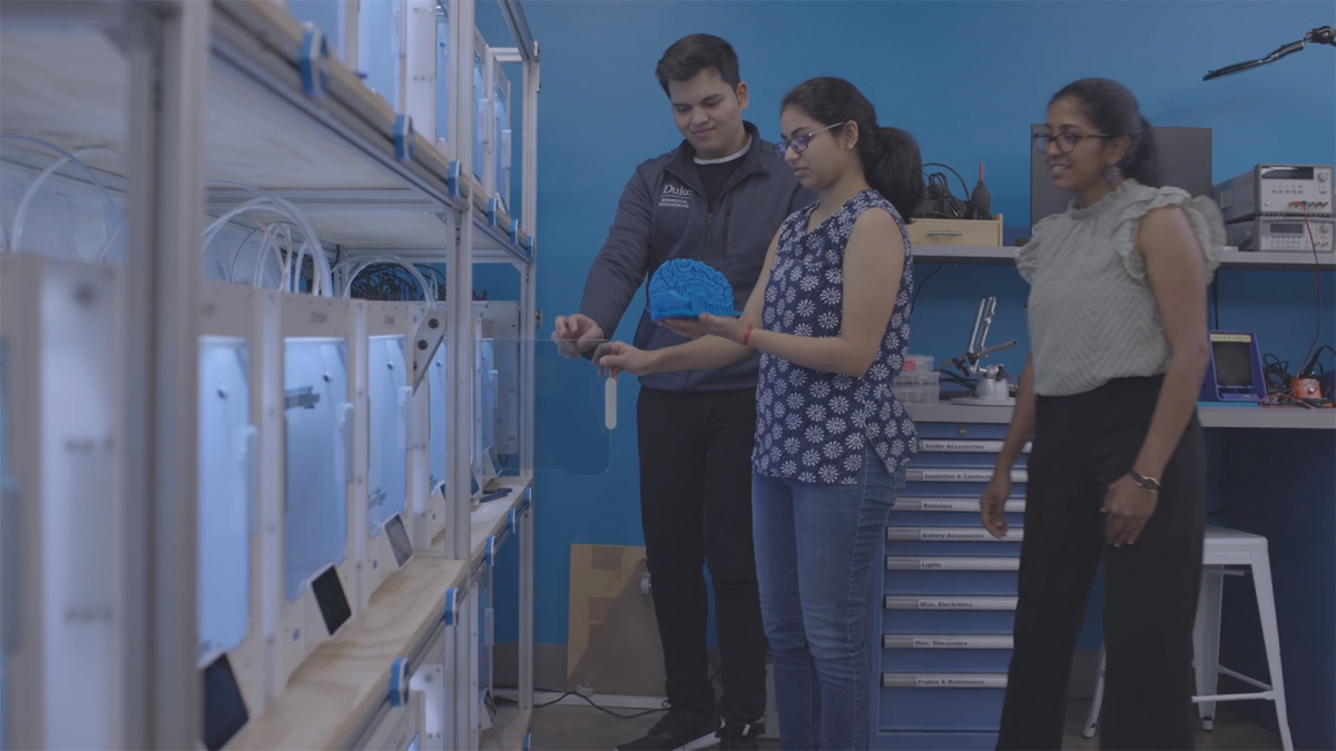 three students at a wall of 3D printers